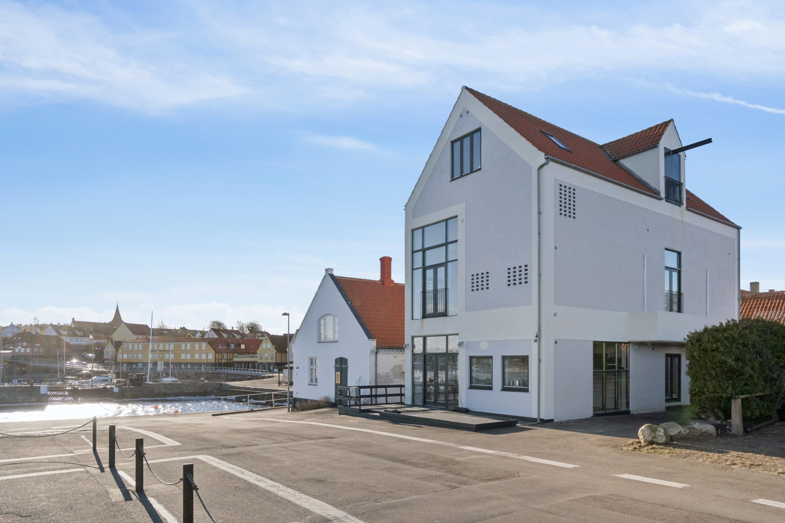 Hvid bygning ved Svaneke Havn med havn og by i baggrunden.